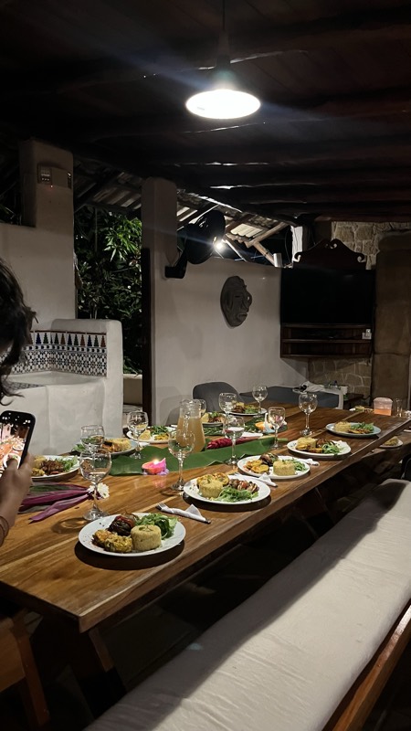 Mesa larga servida de noche para un grupo, con platos y velas.